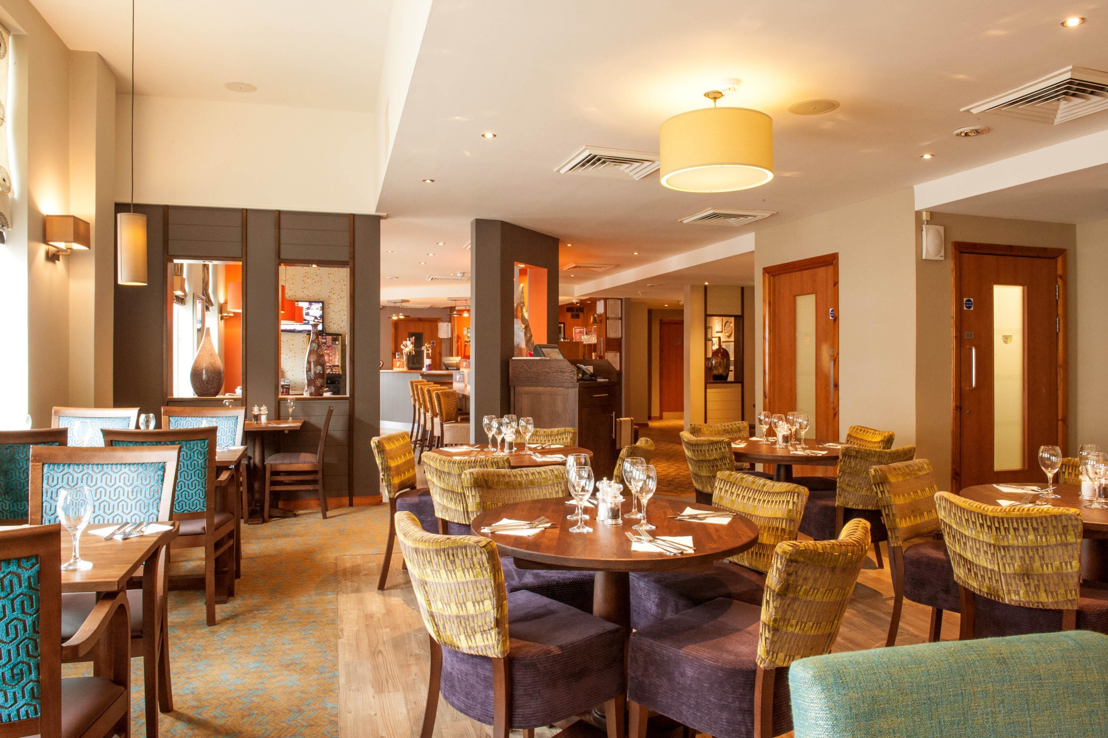 Un comedor de hotel con mesas redondas, sillas y una zona de bar al fondo.
