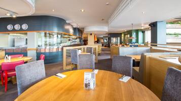 A modern restaurant with round tables, high chairs, and a bar area.