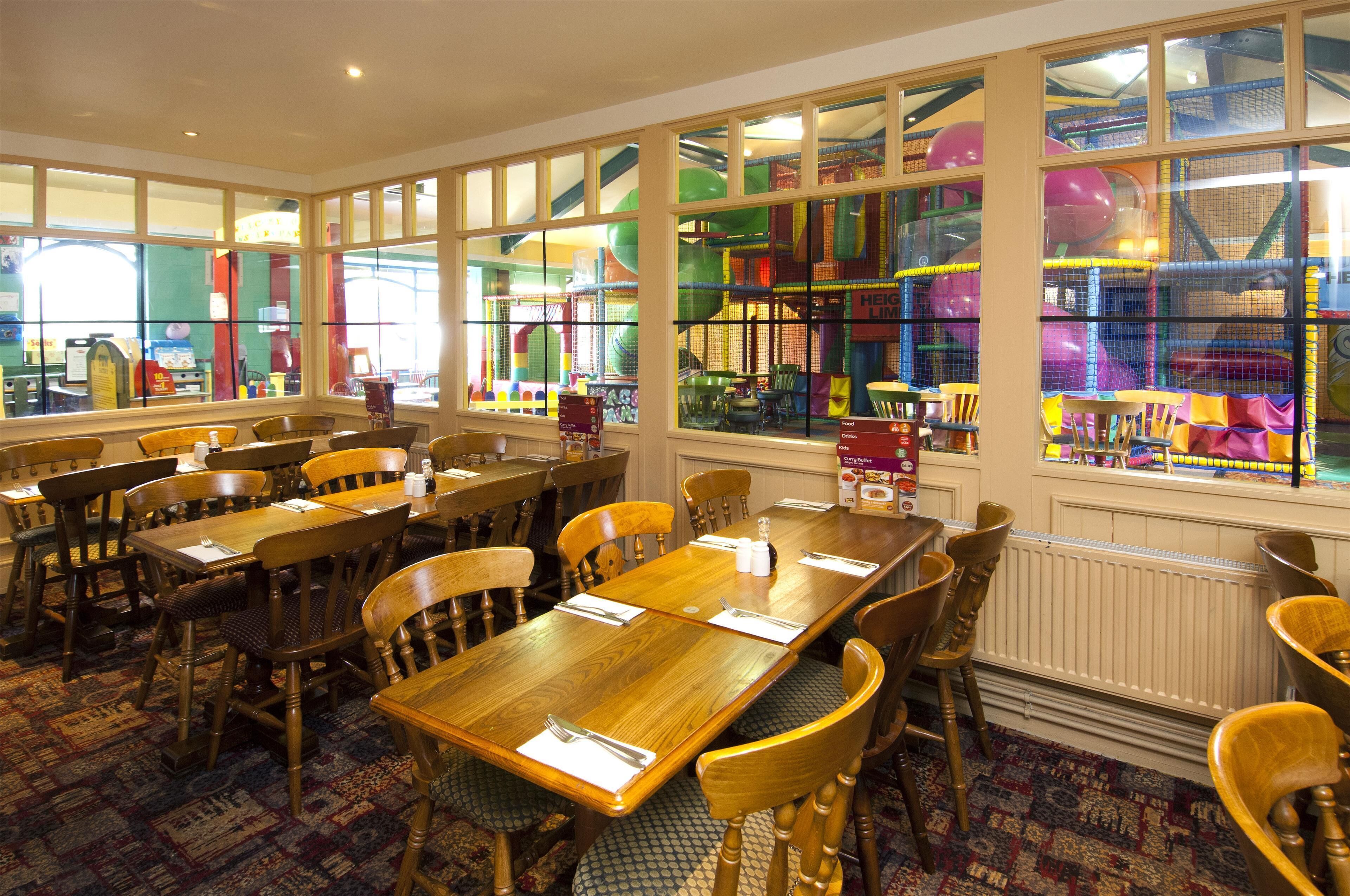 A dining area with wooden tables and chairs, large windows with colorful play structures visible outside.