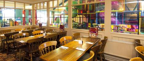 A dining area with wooden tables and chairs, large windows with colorful play structures visible outside.