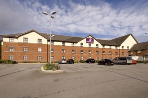 A hotel with a parking lot, a sign for Premier Inn, and a clear sky.