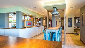 A restaurant interior with a bar area, wooden tables, and blue chairs. - Premier Inn Winchester (Winchester)