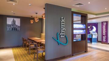 A hotel lobby with a reception desk, a seating area with a table and chairs, and a wall-mounted sign with the hotel's name.