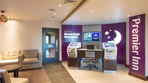 A hotel lobby with a reception desk, check-in kiosks, seating area, and a 'Good Night Guarantee' sign. - Premier Inn Winchester (Winchester)