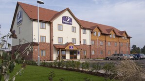 Ein Hotel mit einem gut sichtbaren 'Premier Inn'-Schild, zahlreichen Fenstern und einem Parkplatz mit Autos.