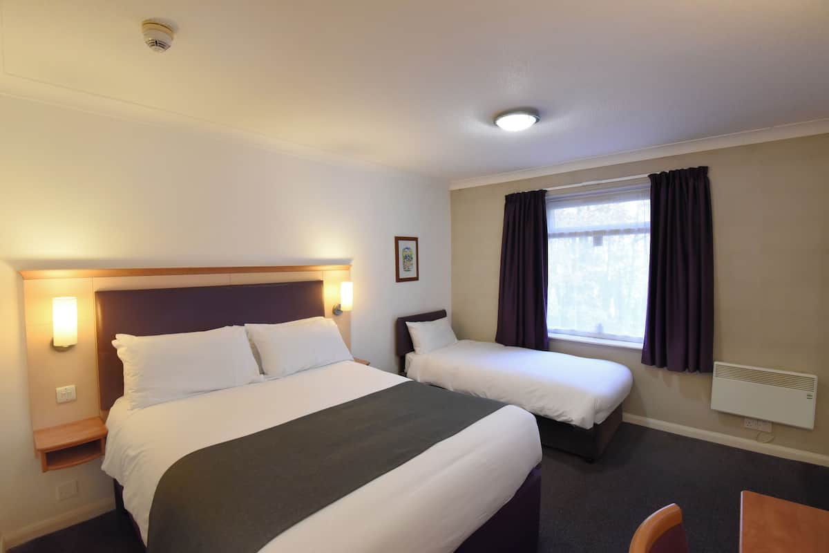 A hotel room with two beds, a nightstand, a desk, and a window with curtains.