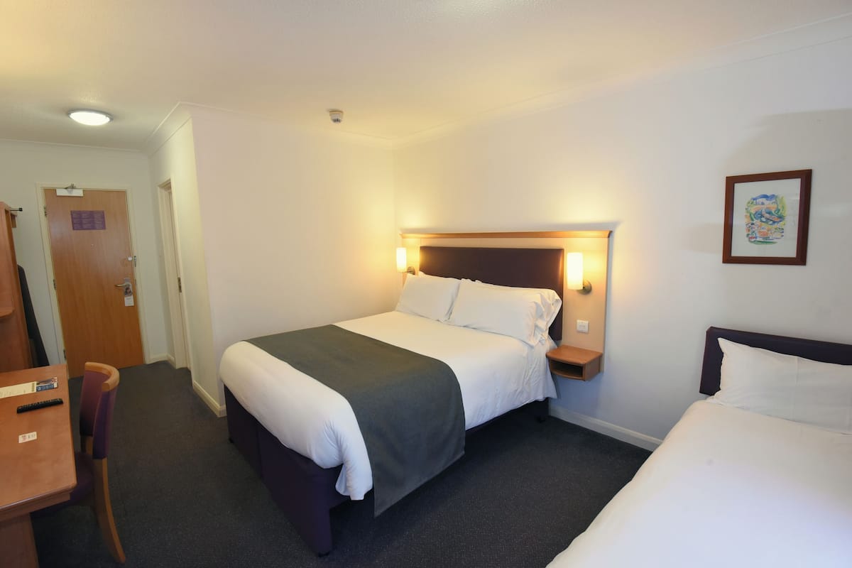 A hotel room with a bed, bedside table, chair, desk, and a door.