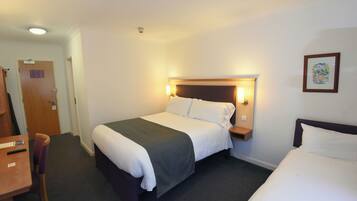 Una habitación de hotel con cama, mesita de noche, silla, escritorio y una puerta.