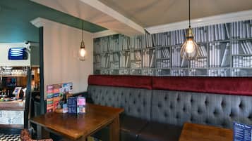 A cozy bar area with a wooden counter, a cushioned bench, and a wall with bookshelves.