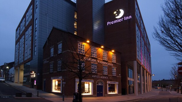 Um hotel com uma placa Premier Inn bem visível, fachada de tijolos tradicionais e um edifício moderno em vidro.