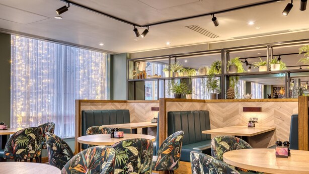 A restaurant with round tables, booths, and tropical-themed chairs. - Premier Inn Aldershot (Aldershot)