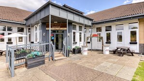 A building with a tiled roof, a covered entrance, and outdoor seating. - Premier Inn Basingstoke West (Basingstoke)