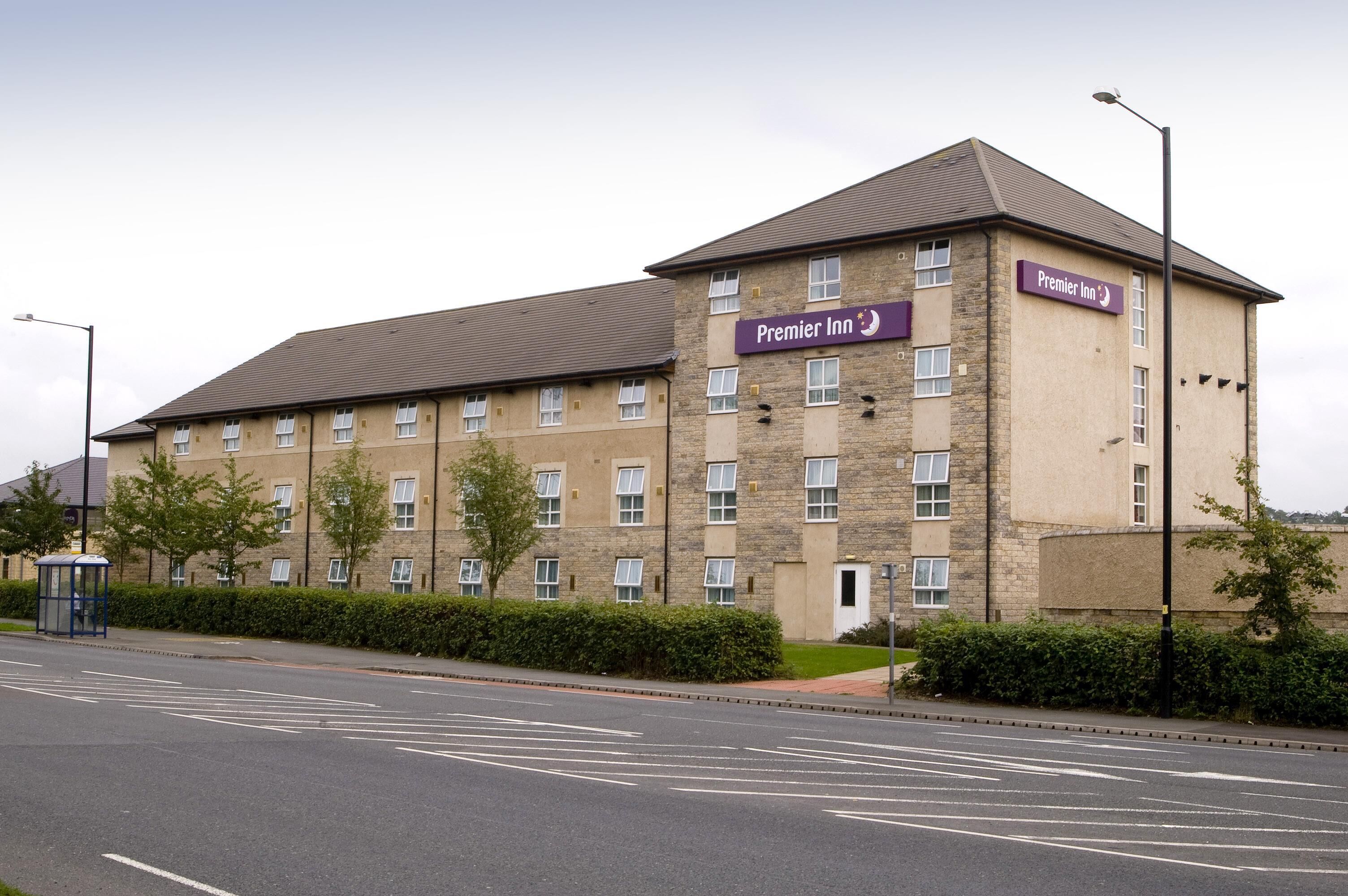 A multi-story hotel with a stone facade, a prominent sign for Premier Inn, and a clear road in front.