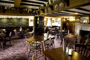 L’intérieur d’un pub traditionnel, avec des tables et des chaises en bois, un tableau noir servant de menu et une cheminée en briques.
