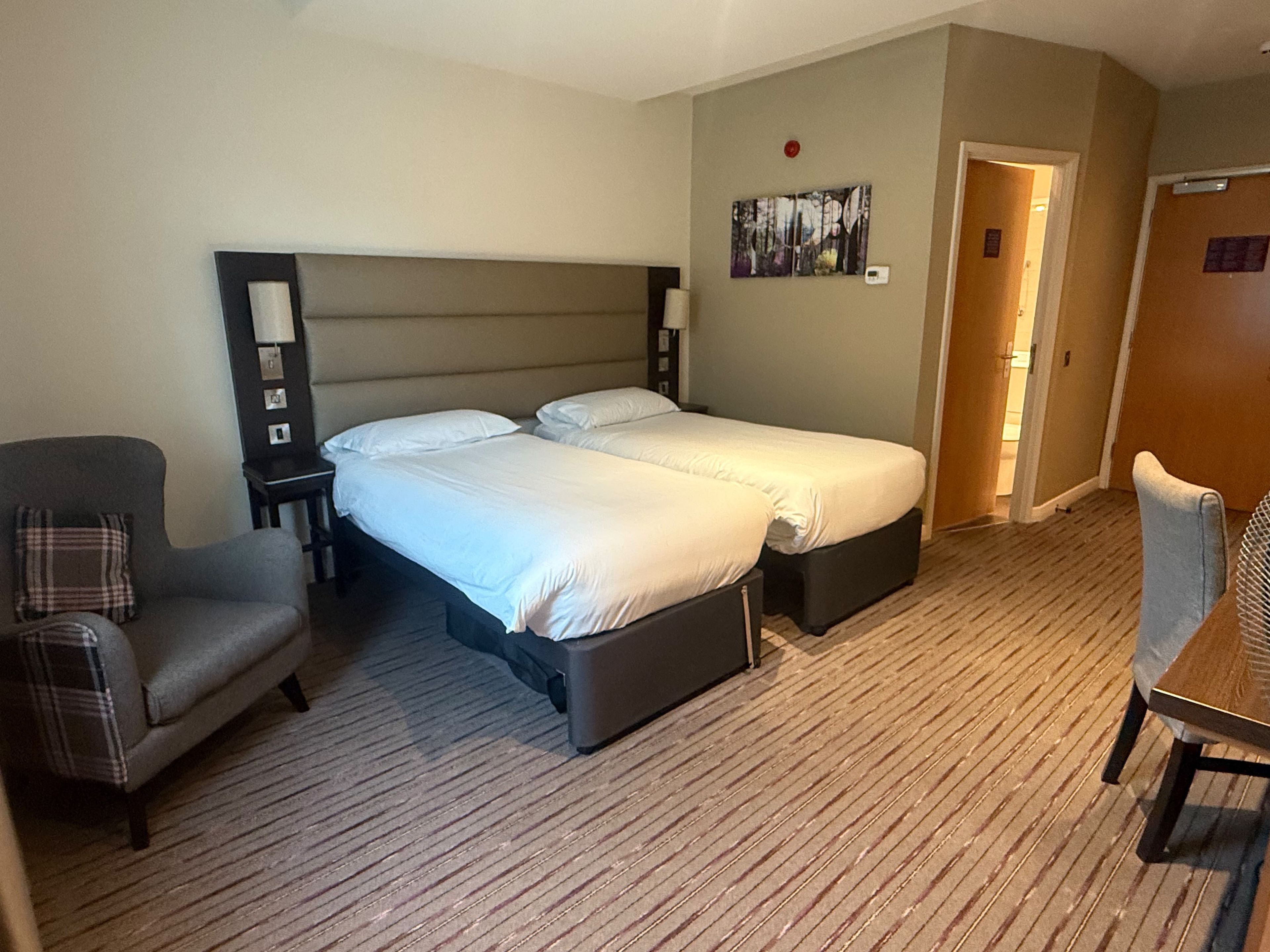 Une chambre d’hôtel avec un lit double, une chaise, un bureau et un tableau au mur.