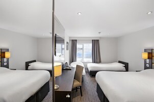 A hotel room with two beds, a desk with a chair, a large mirror, and a window with curtains.