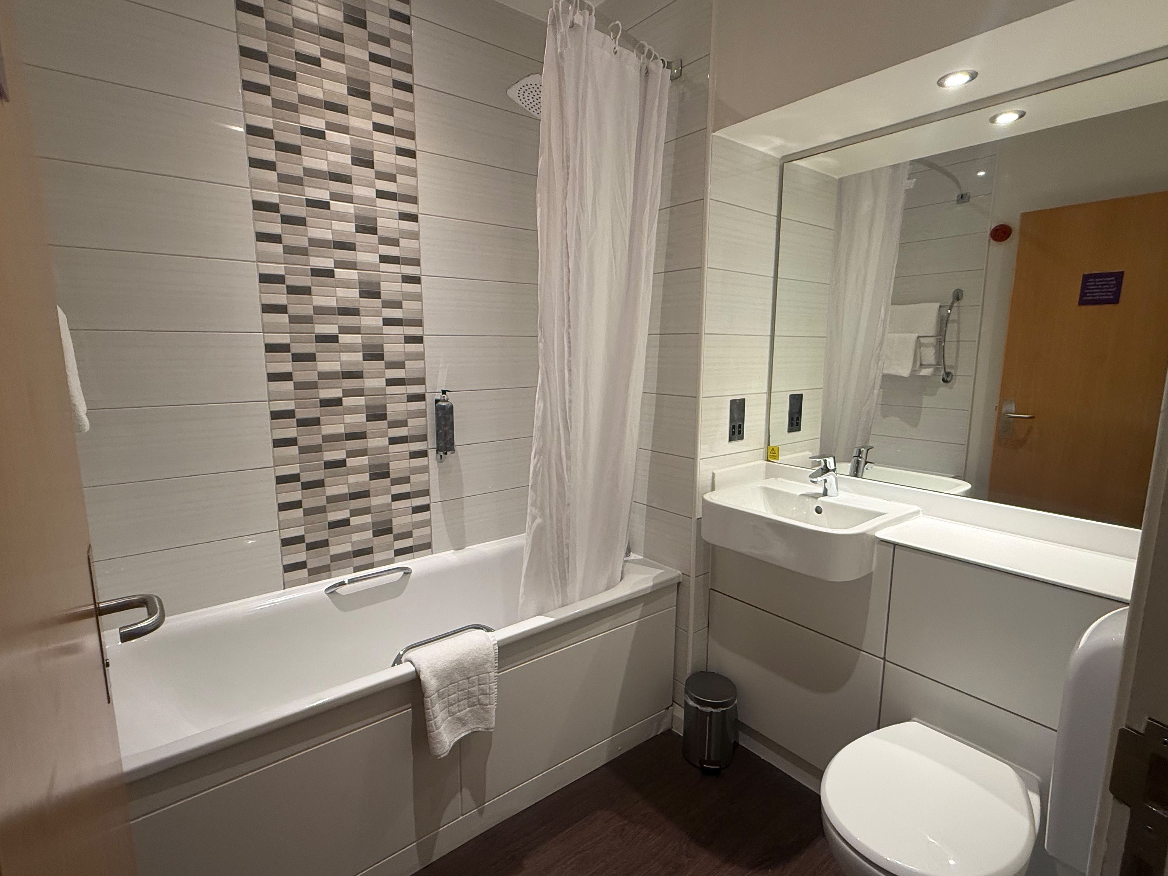 A modern bathroom with a bathtub, a sink, a toilet, and a mirror.