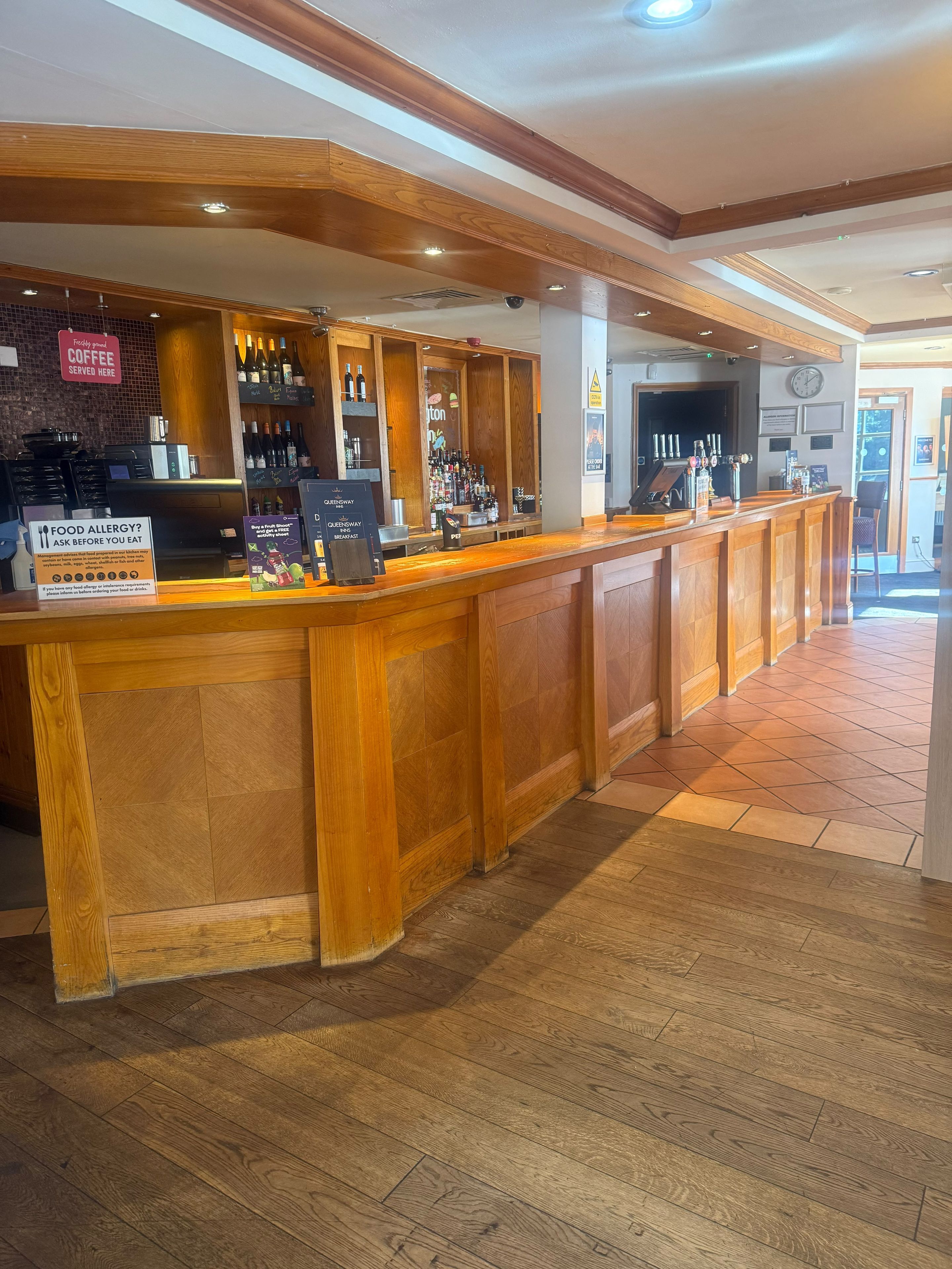 Zona de bar con mostrador de madera, estanterías con botellas y un letrero que indica servicio de café.