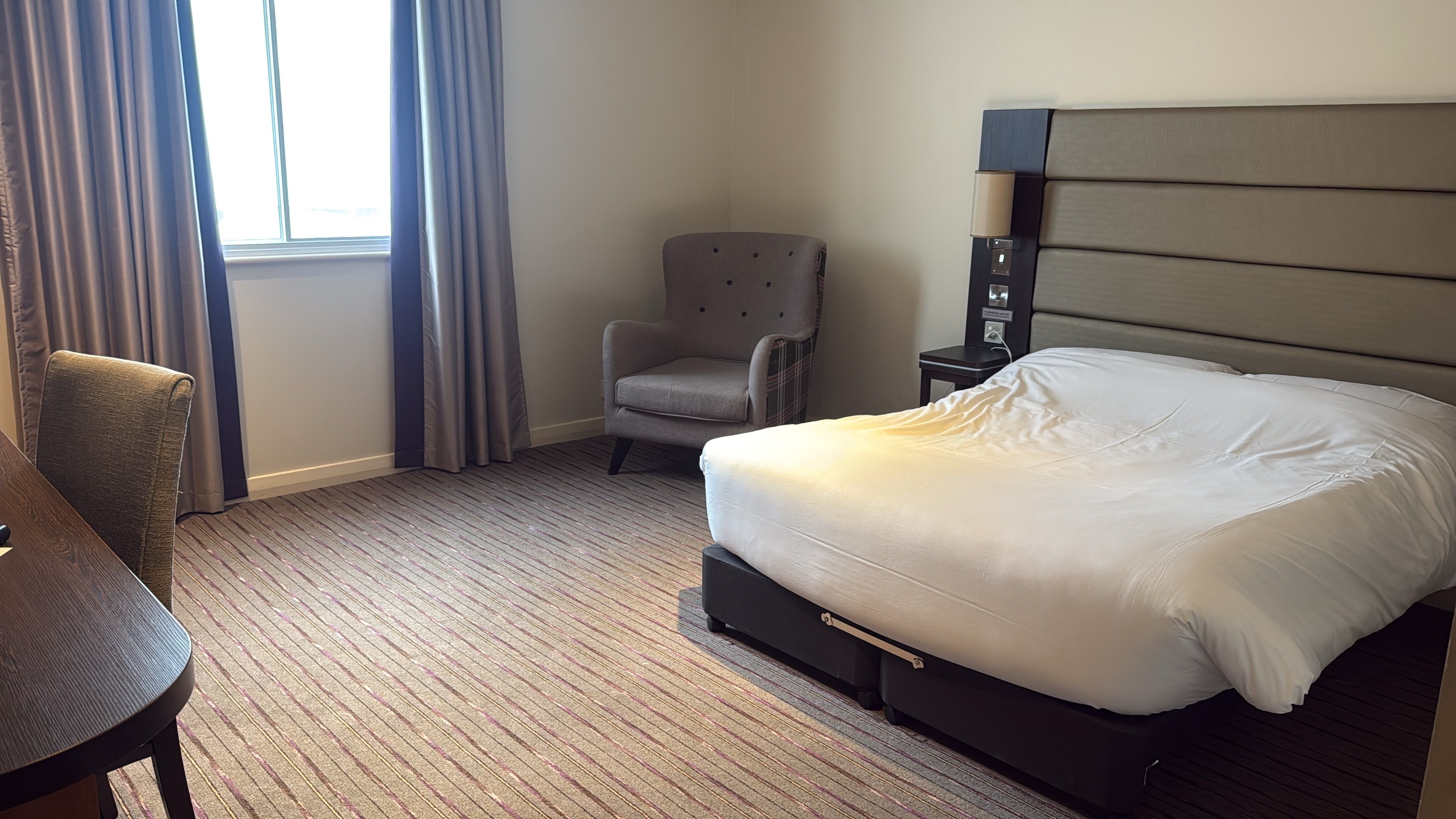 A hotel room with a bed, a chair, a desk, and a lamp.