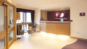 Een receptie met een 'Premier Inn'-bord, een receptiebalie, een zithoek met stoelen en uitzicht door een glazen deur.