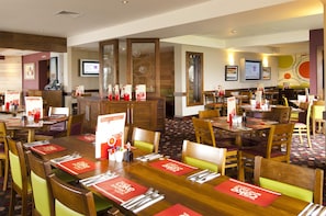 A hotel restaurant with multiple dining tables, chairs, and a counter with a menu display. - Premier Inn Widnes (Widnes)