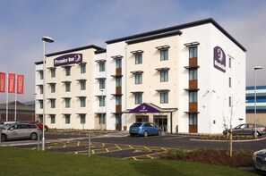 Ein mehrstöckiges Hotel mit einem gut sichtbaren 'Premier Inn'-Schild, einem Parkplatz und blauem Himmel.