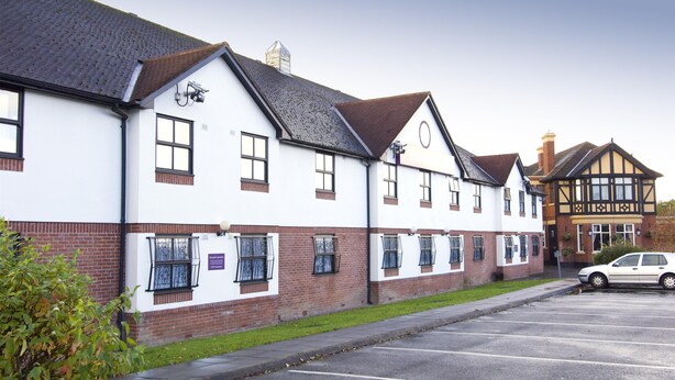 A building with a white facade, multiple windows, a parking lot, and a car parked in front. - Premier Inn Manchester Airport Heald Green (Cheadle)