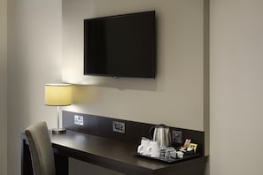 A hotel room with a flat-screen TV, a desk with a lamp, a chair, a tray with coffee cups and a kettle, and a wall-mounted control panel. - Premier Inn Telford Central (Telford)