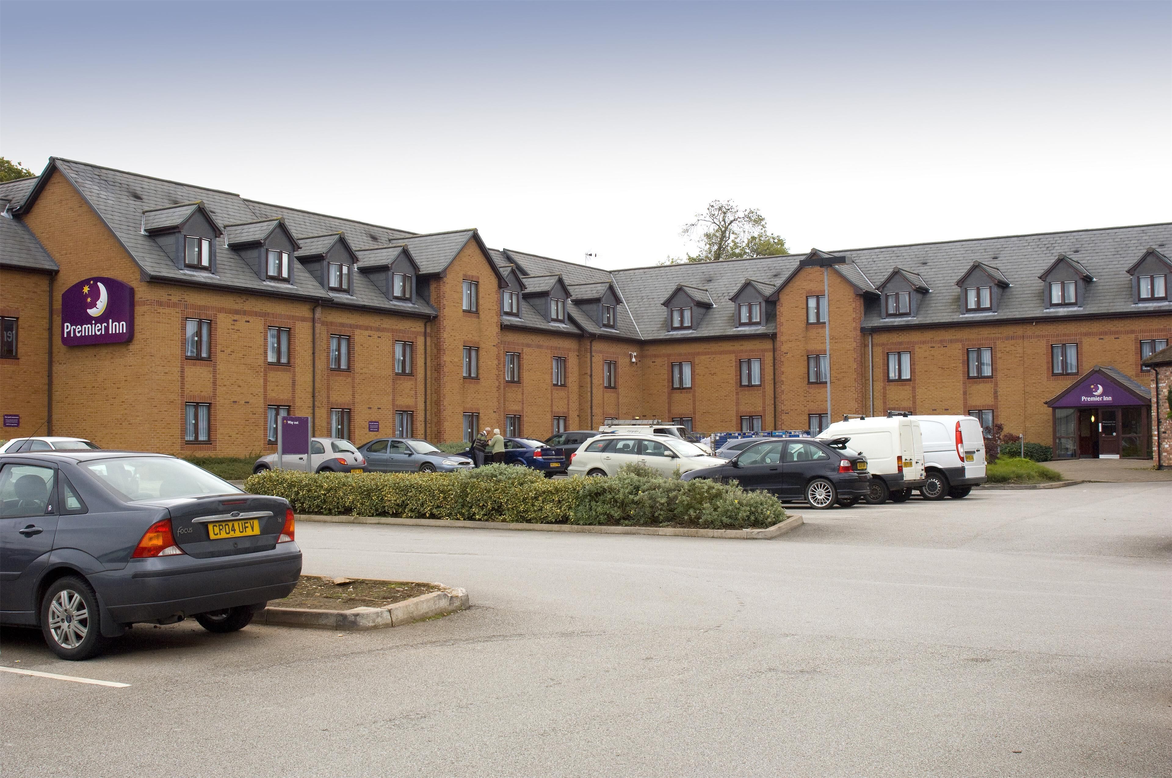 Een Premier Inn hotel met een gevel van baksteen, meerdere ramen en een parkeerplaats met auto's en een bestelwagen.