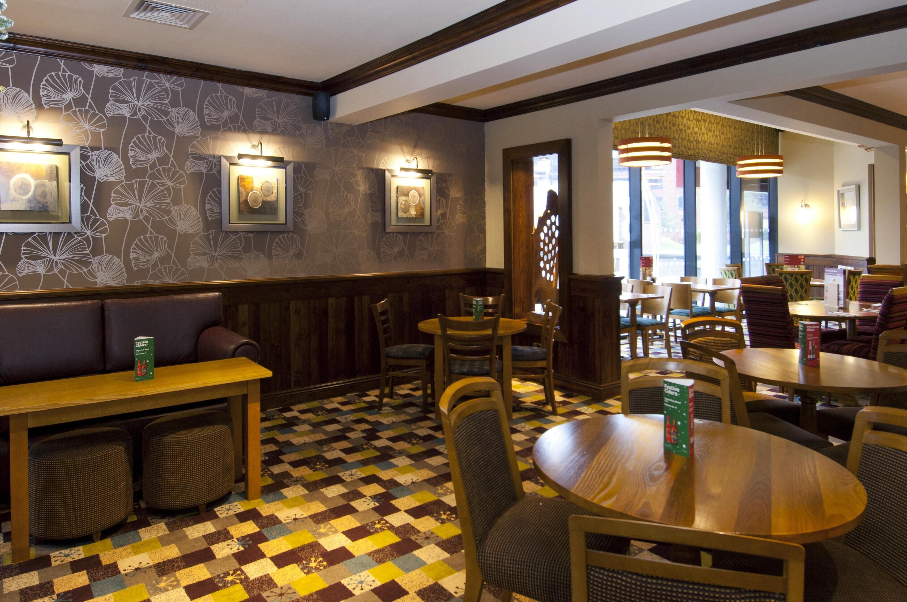 L’intérieur d’un restaurant est décoré de papier peint à motifs, de tables et de chaises en bois, et les murs sont ornés de tableaux encadrés.