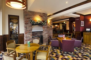 Un pub acogedor con chimenea de ladrillo, mesas de madera y sillas moradas.