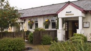 A building with a 'Welcome' sign, a wooden fence, and hanging flower baskets. - Premier Inn Stirling South - M9 J9 (Stirling)