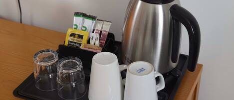 A tray with a stainless steel kettle, two white mugs, two shot glasses, a spoon, and a pack of Twinings tea bags.