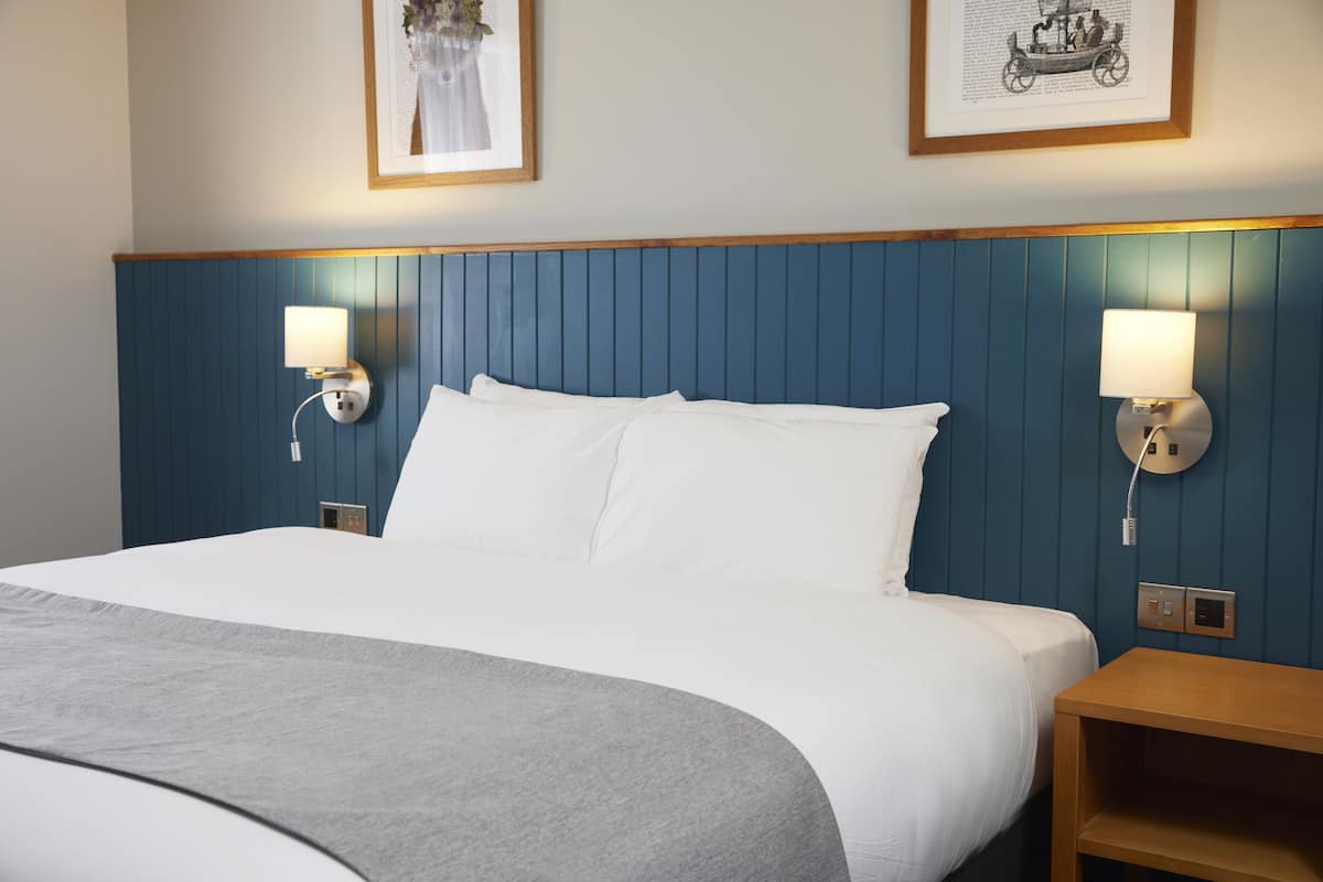 A neatly made bed with white linens, a wooden headboard, and two wall-mounted lamps on either side.