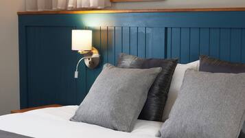 Una habitación de hotel con cama, almohadas, una lámpara de pared y un cuadro enmarcado sobre la cama.