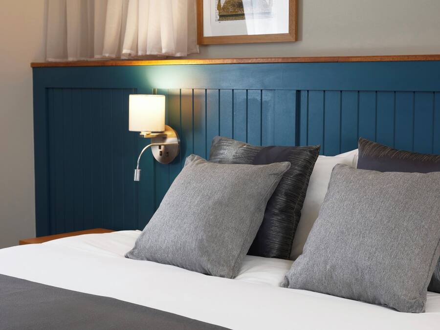 Una habitación de hotel con cama, almohadas, una lámpara de pared y un cuadro enmarcado sobre la cama.