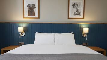 Quarto de hotel com uma cama grande, duas luminárias fixadas na parede e duas fotografias emolduradas.