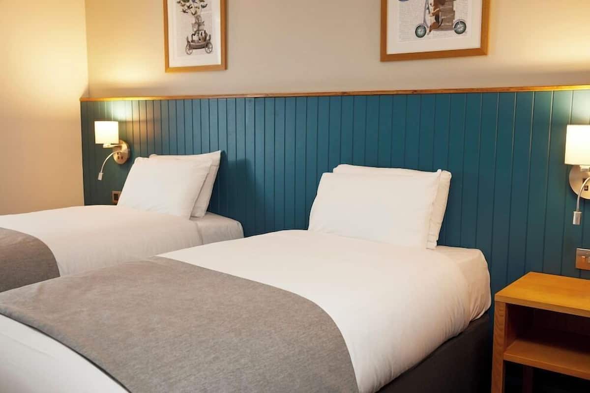 A hotel room with two beds, a wooden nightstand, and wall-mounted lamps.