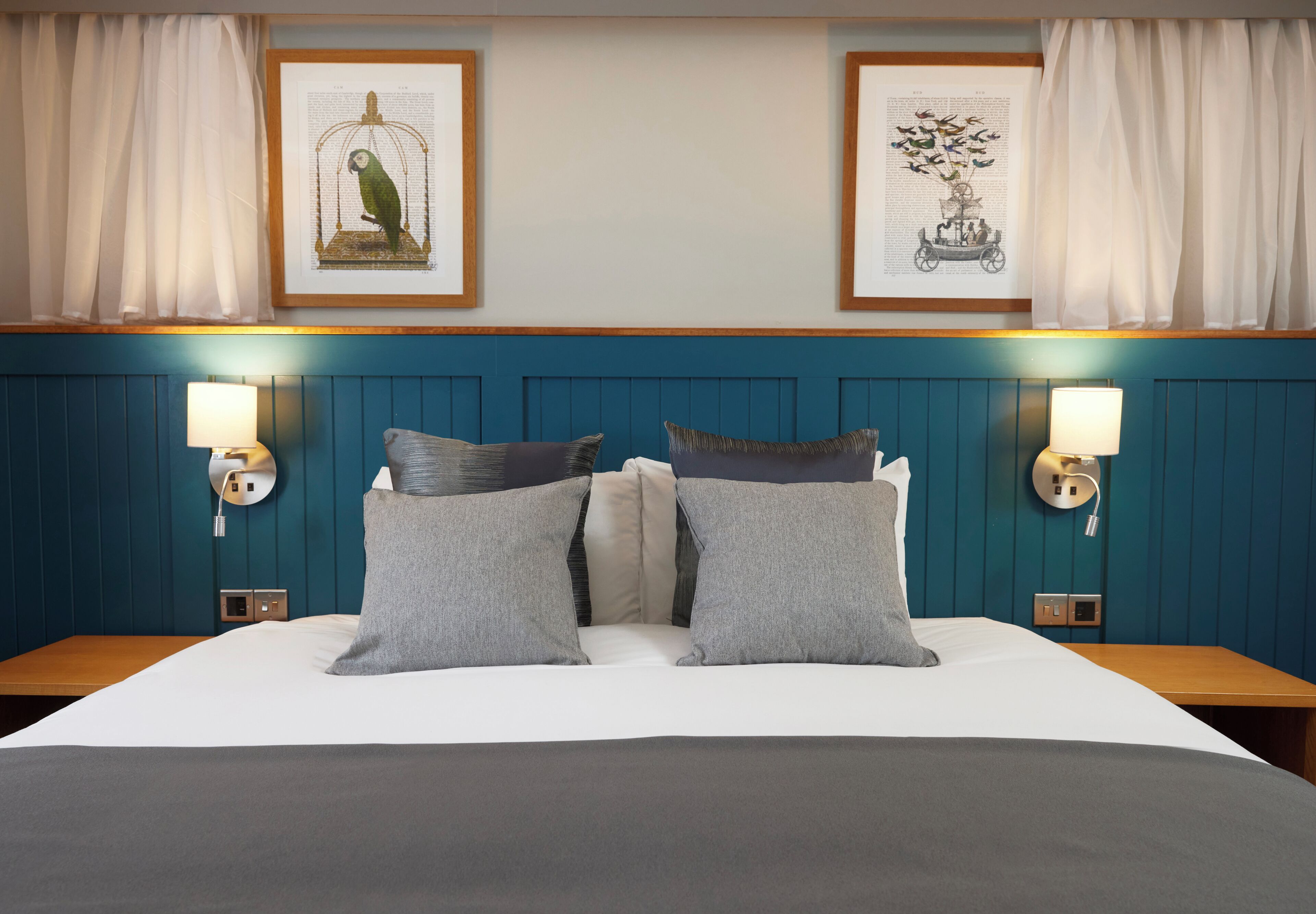 A hotel room with a bed, two wall-mounted lamps, and two framed pictures on the wall.