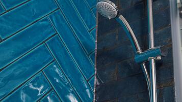A shower with a chrome handle and a handheld showerhead, set against a blue tiled wall.