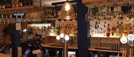 A bar area with shelves of liquor bottles, a cash register, and a menu board.