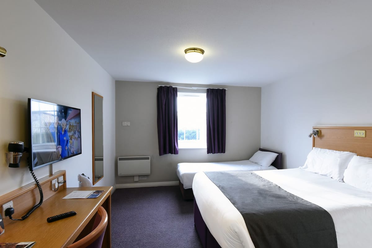 Habitación de hotel con cama, escritorio con teléfono, televisión, ventana con cortinas e iluminación en el techo.