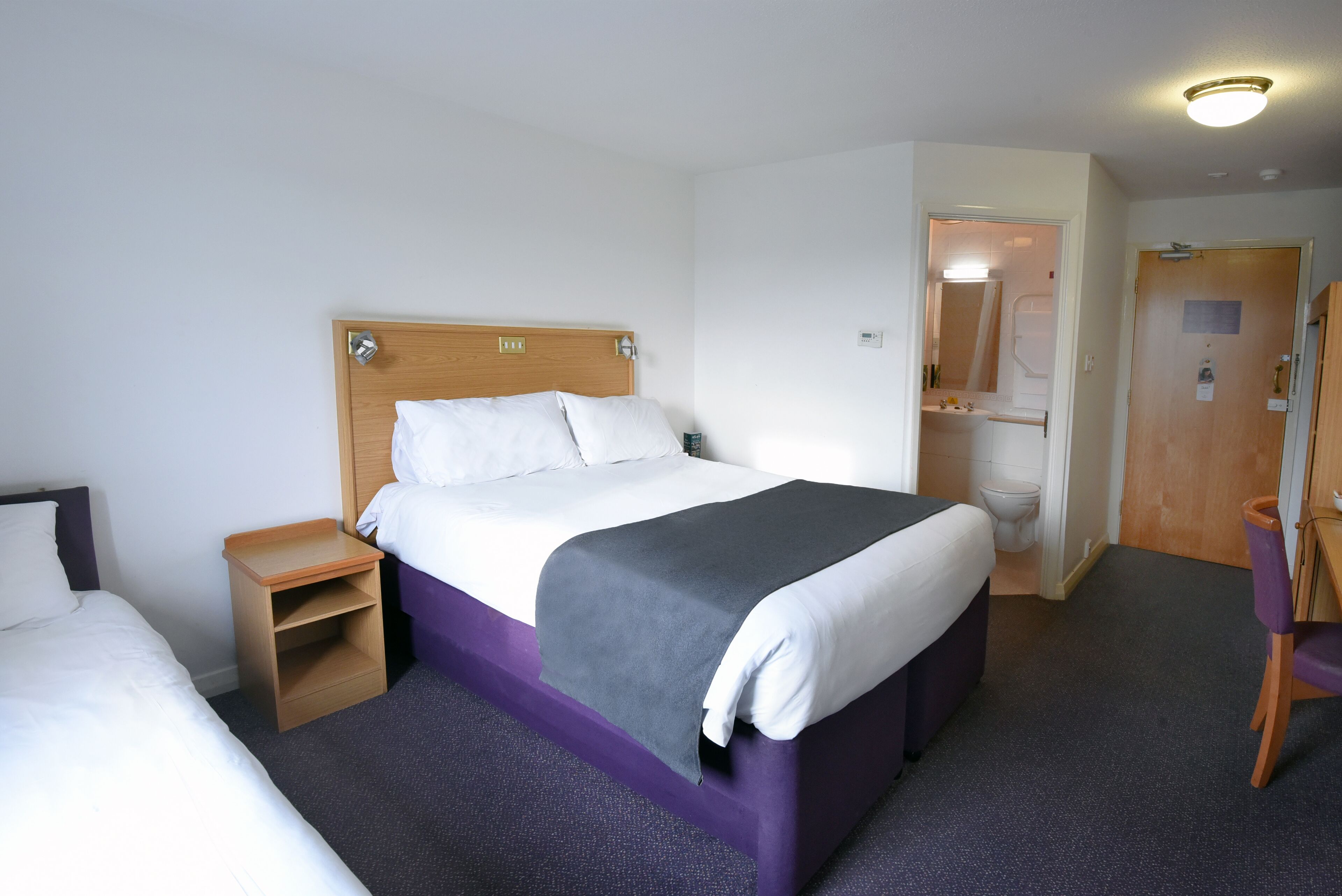 A hotel room with a bed, a nightstand, a chair, and a bathroom visible through an open door.