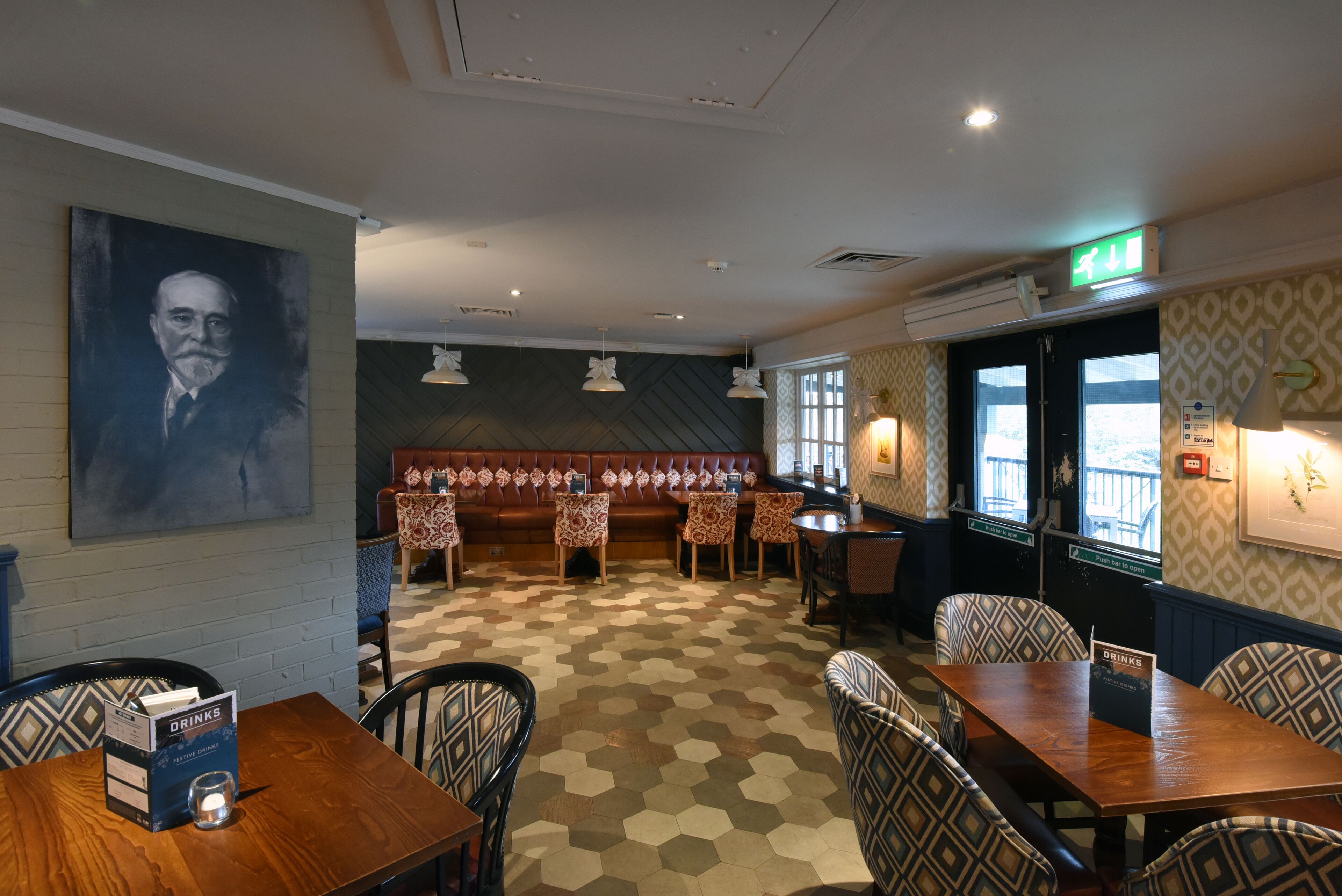 A restaurant with hexagonal patterned flooring, a large portrait on the wall, and a seating area with patterned chairs and tables.