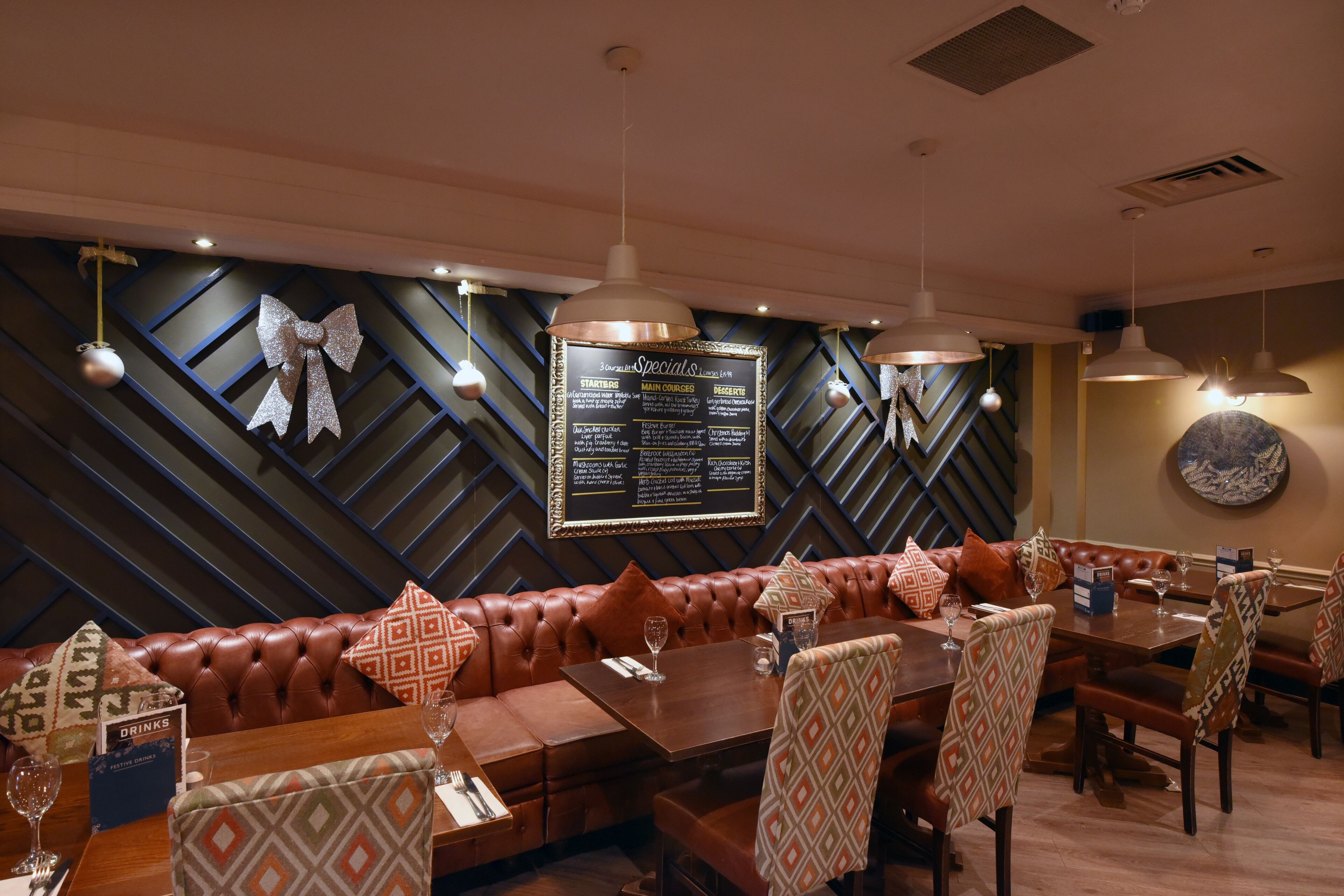 A restaurant interior with a long brown leather booth, patterned chairs, and a menu board on the wall.