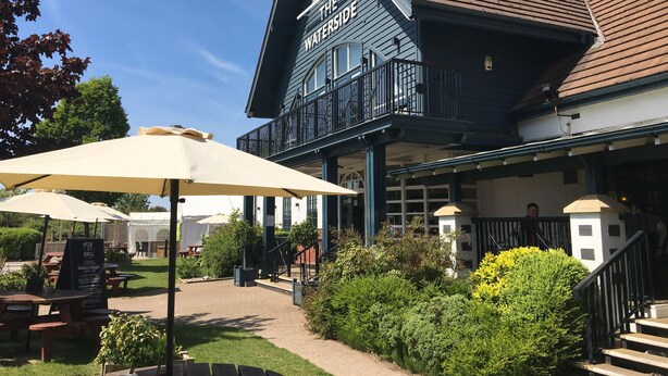 Un edificio con un letrero que dice "The Waterside Pub & Grill", con mesas al aire libre y un patio cubierto.