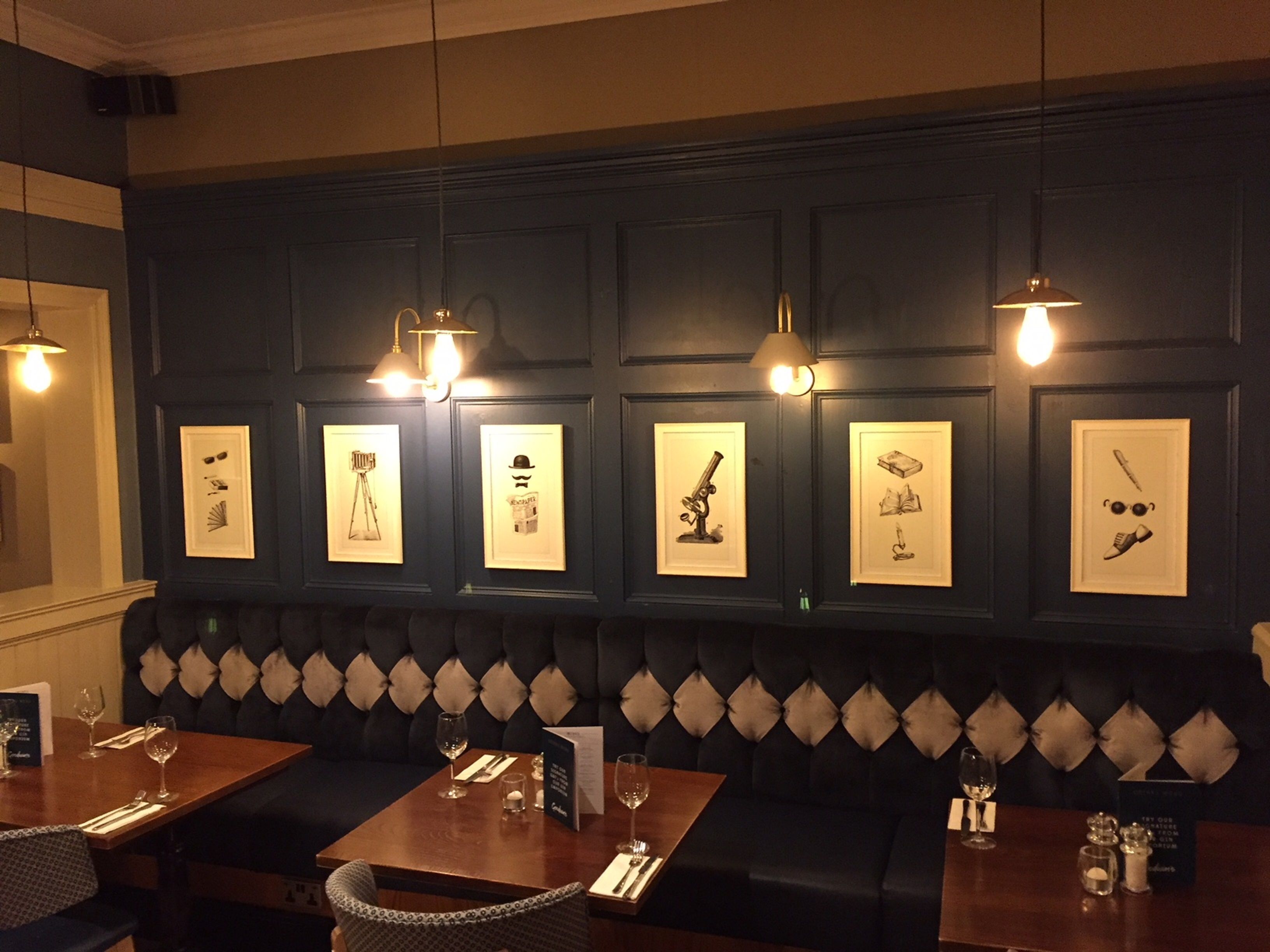 A restaurant interior with dark wooden paneling, a tufted black bench, and framed artwork on the wall.