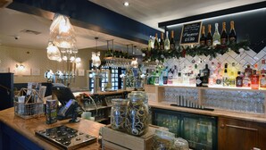 Zona de bar con caja registradora, estantes llenos de botellas y una exhibición de vasos.