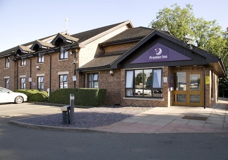 A brick building with a 'Premier Inn' sign, a parking lot, and a sidewalk.. Premier Inn Wellingborough