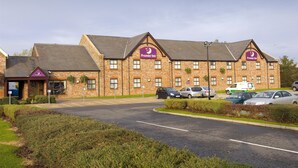 A brick building with a sign for Premier Inn, a parking lot, and several cars. - Premier Inn Wigan - M6 J25 (Wigan)